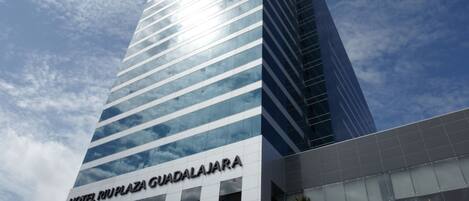 Un moderno edificio de hotel con fachada de vidrio y un letrero que dice "HOTEL MUPLAZA GUADALAJARA".