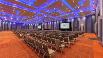A conference room with rows of chairs, a large screen, and a 'RIU Plaza' sign.