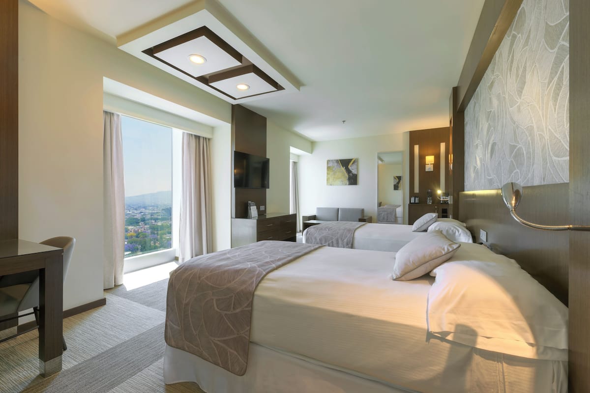 Une chambre d’hôtel avec deux lits, un bureau, une télévision et une grande fenêtre donnant sur la ville.