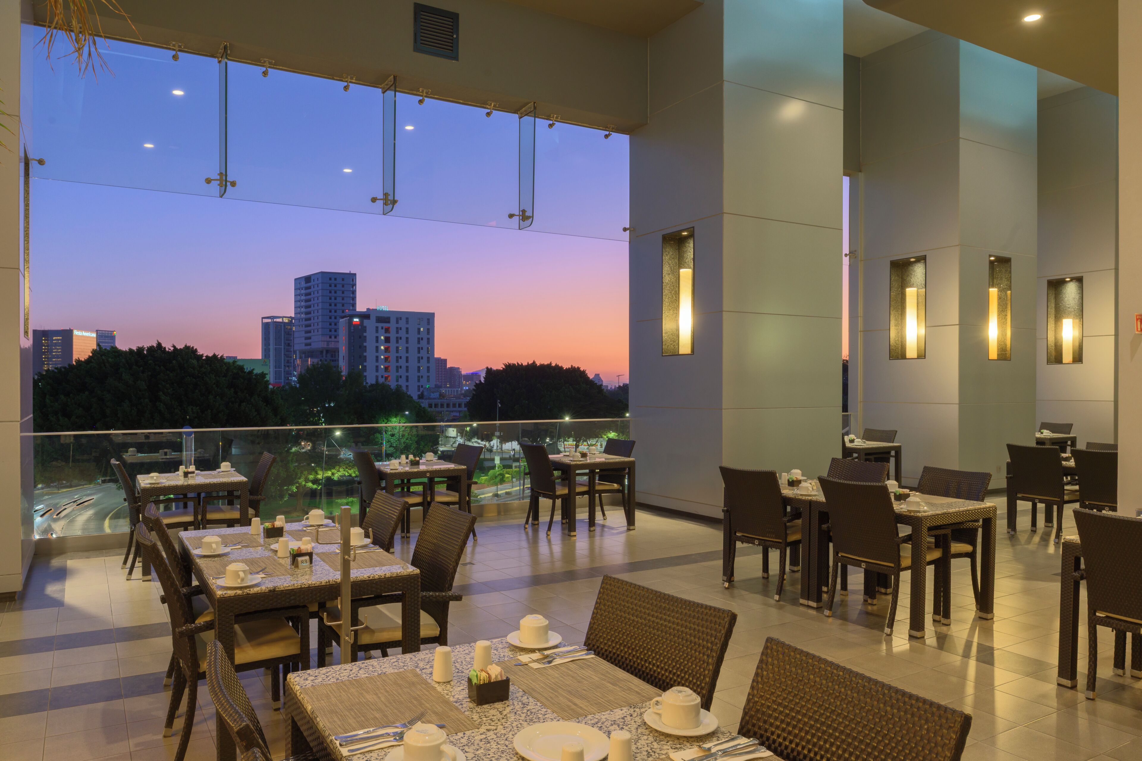 Ein Restaurant mit gedeckten Tischen, Blick auf die Stadt und modernen Leuchten.
