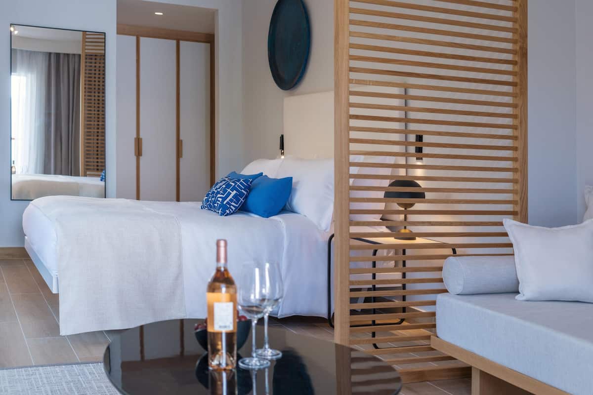 Ein modernes Hotelzimmer mit Bett, Sofa, Tisch mit Flasche und Gläsern sowie einer Holzwand.