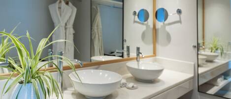 A modern bathroom with a large mirror, two sinks, and a potted plant.