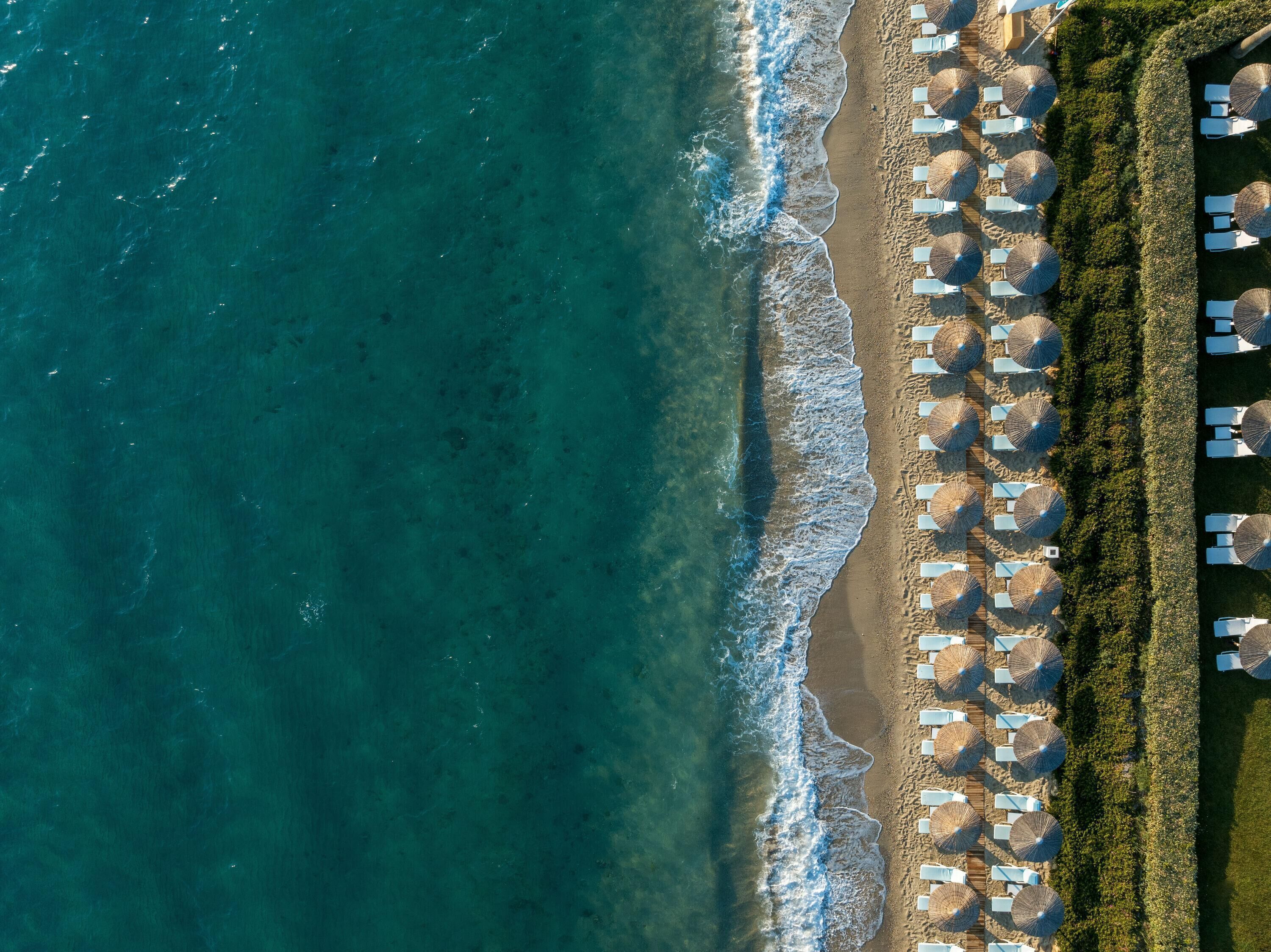 An aerial view of a beach with rows of sun loungers and umbrellas, indicating a resort setting.
