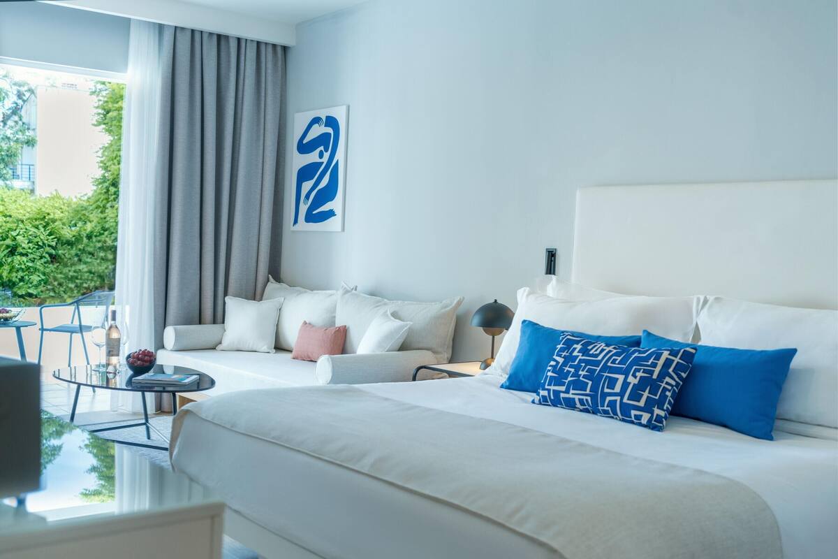 Ein modernes Hotelzimmer mit einem großen Bett, einer Sitzecke, einem kleinen Tisch und Blick auf Grünflächen.