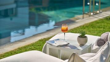 Zona de descanso junto a la piscina con una bebida de naranja, una revista y una planta en maceta sobre una mesita.