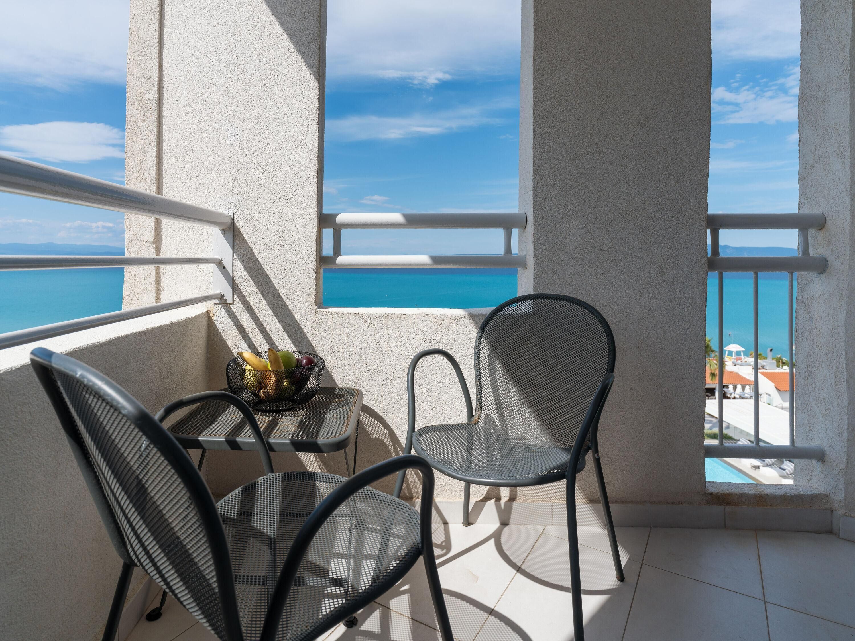 A balcony with two chairs, a small table with fruit, and a view of the sea.