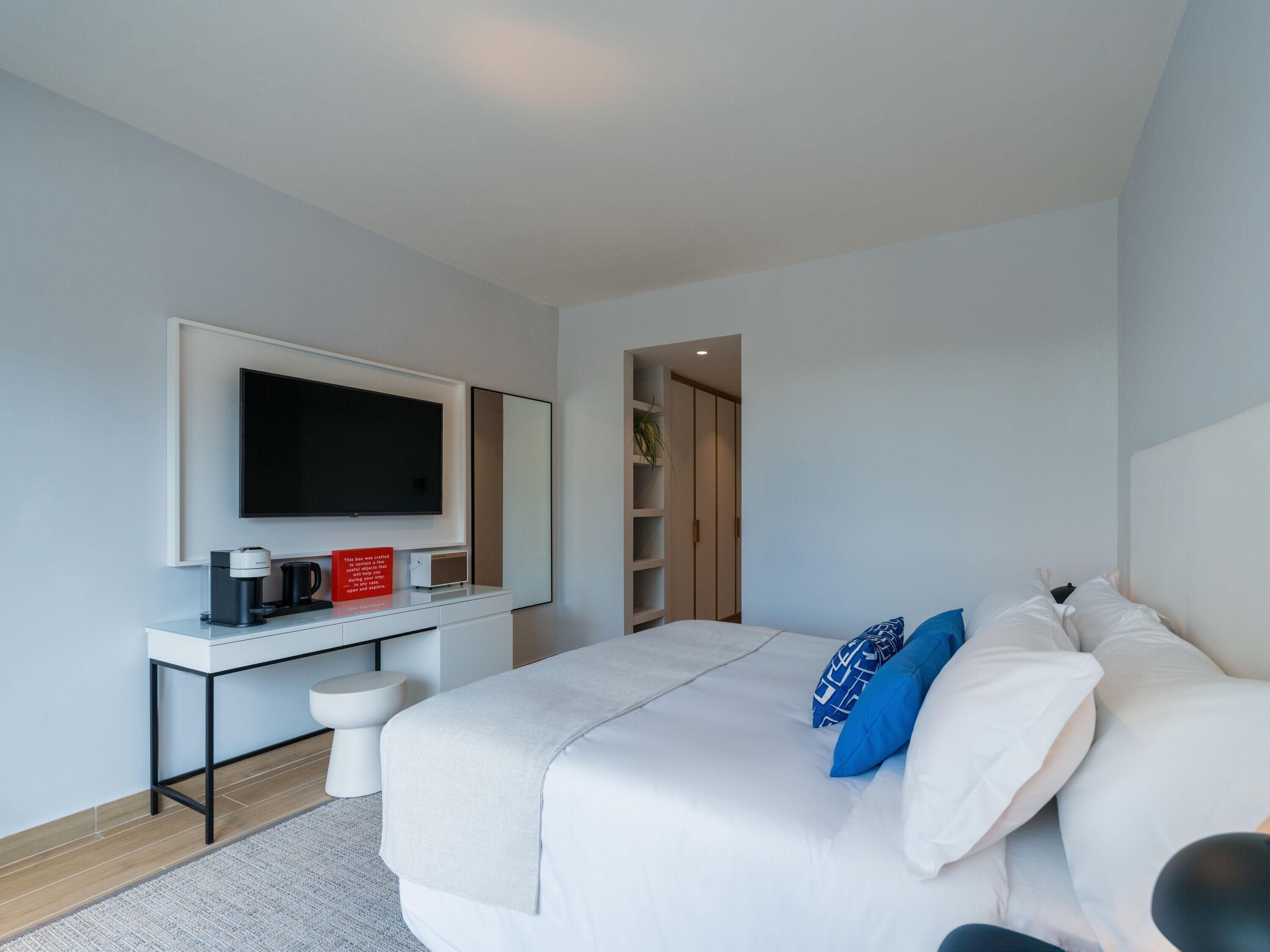 Una habitación de hotel moderna con una cama, un escritorio con cafetera, un televisor de pantalla plana y un vestidor.