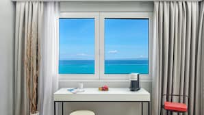 A hotel room with a desk, a coffee maker, a fruit bowl, a chair, and a view of the ocean.