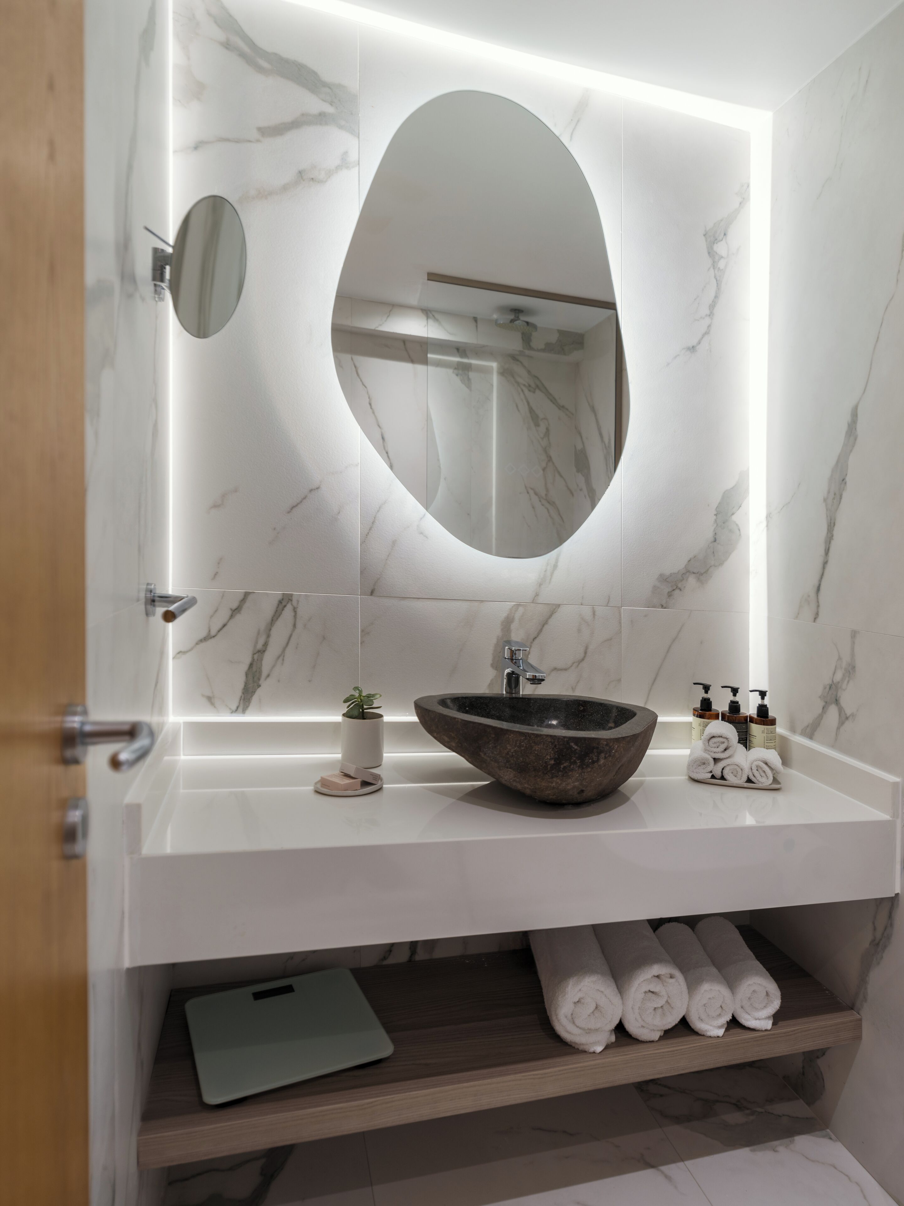 Een moderne badkamer met een marmeren wastafelmeubel, een grote ovale spiegel en een inloopdouche.