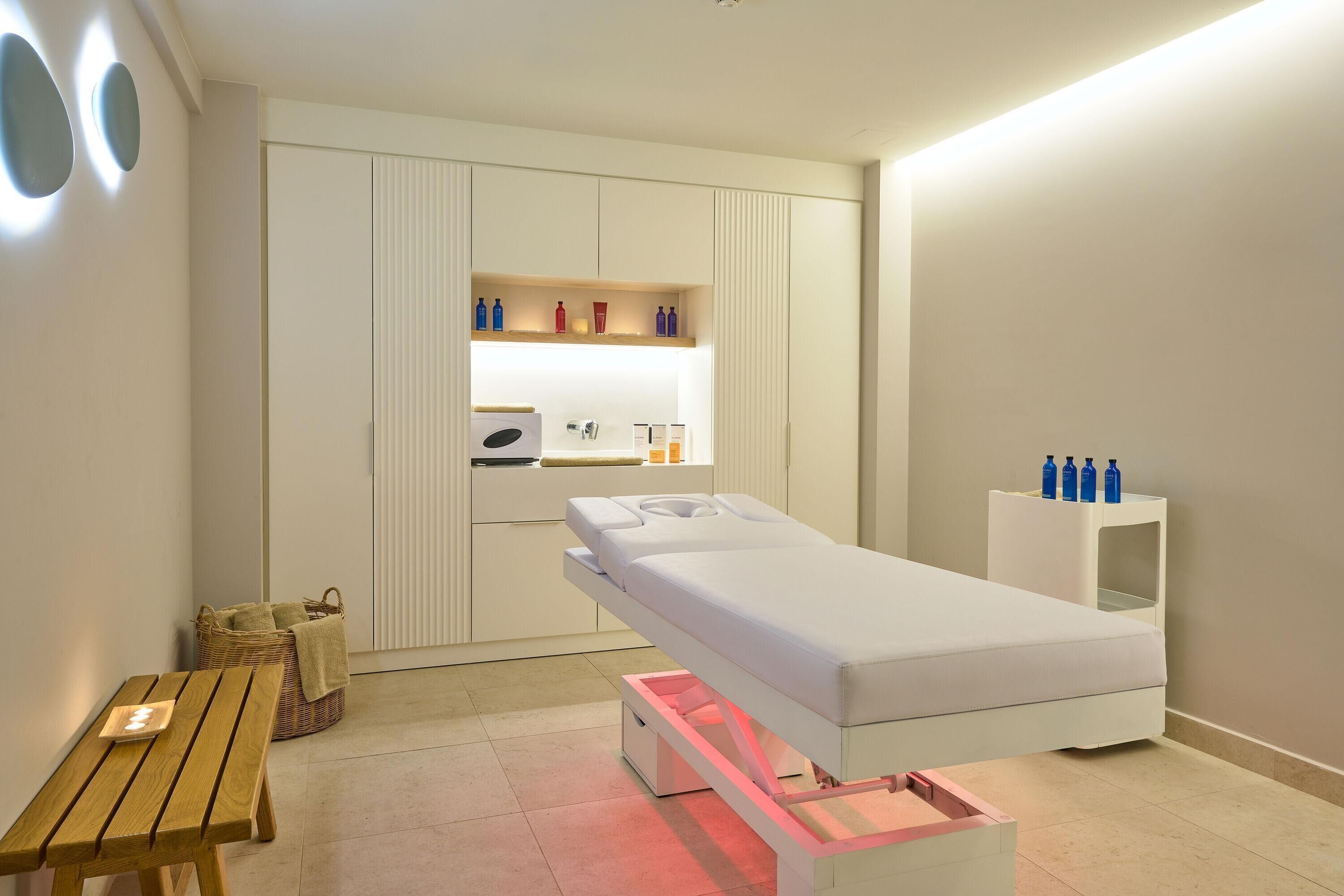 Una habitación moderna con una camilla de masaje, una mesita de madera, una cesta y un estante con botellas.