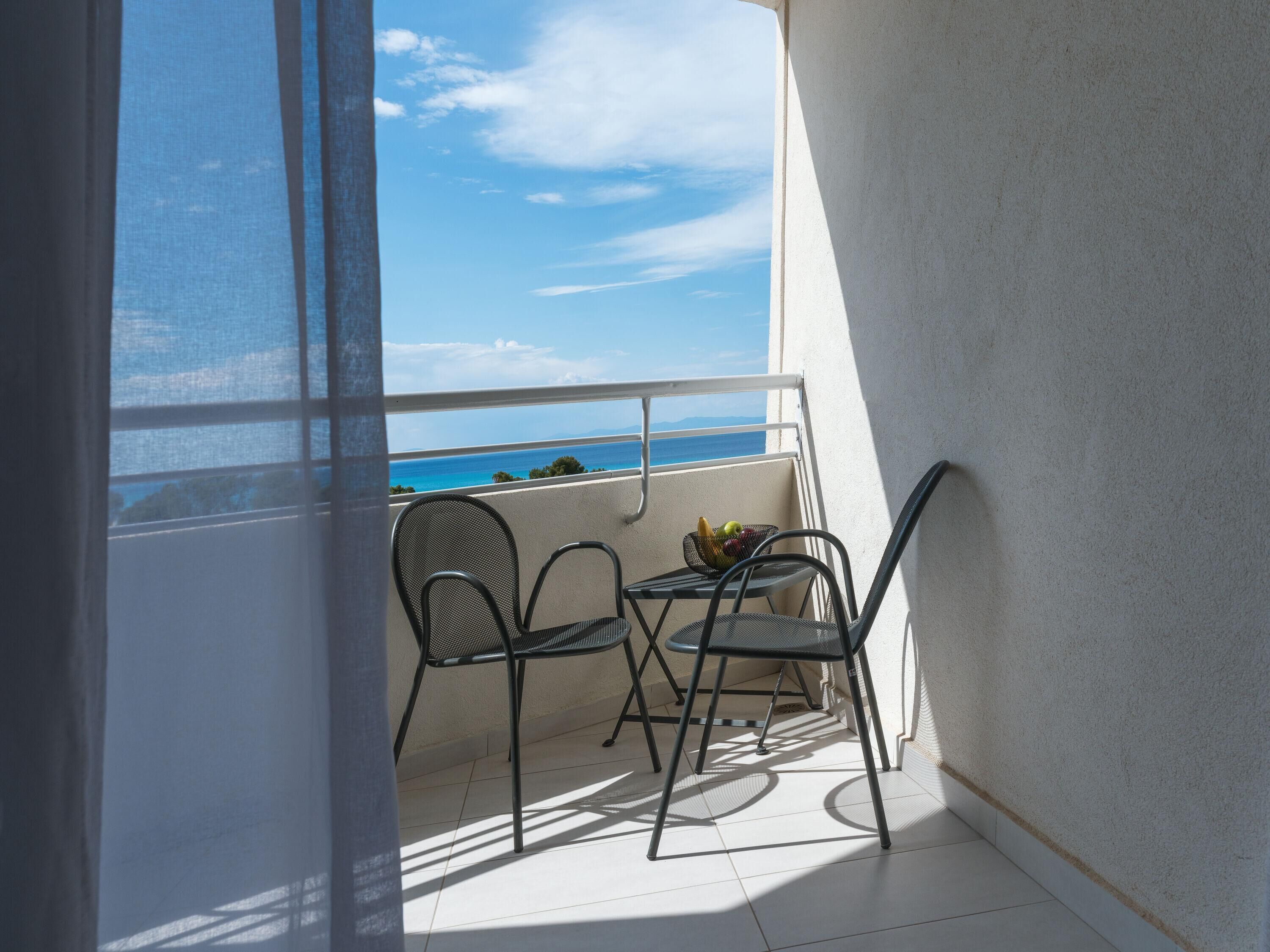 Un balcon avec deux chaises et une petite table, offrant une vue panoramique sur la mer.