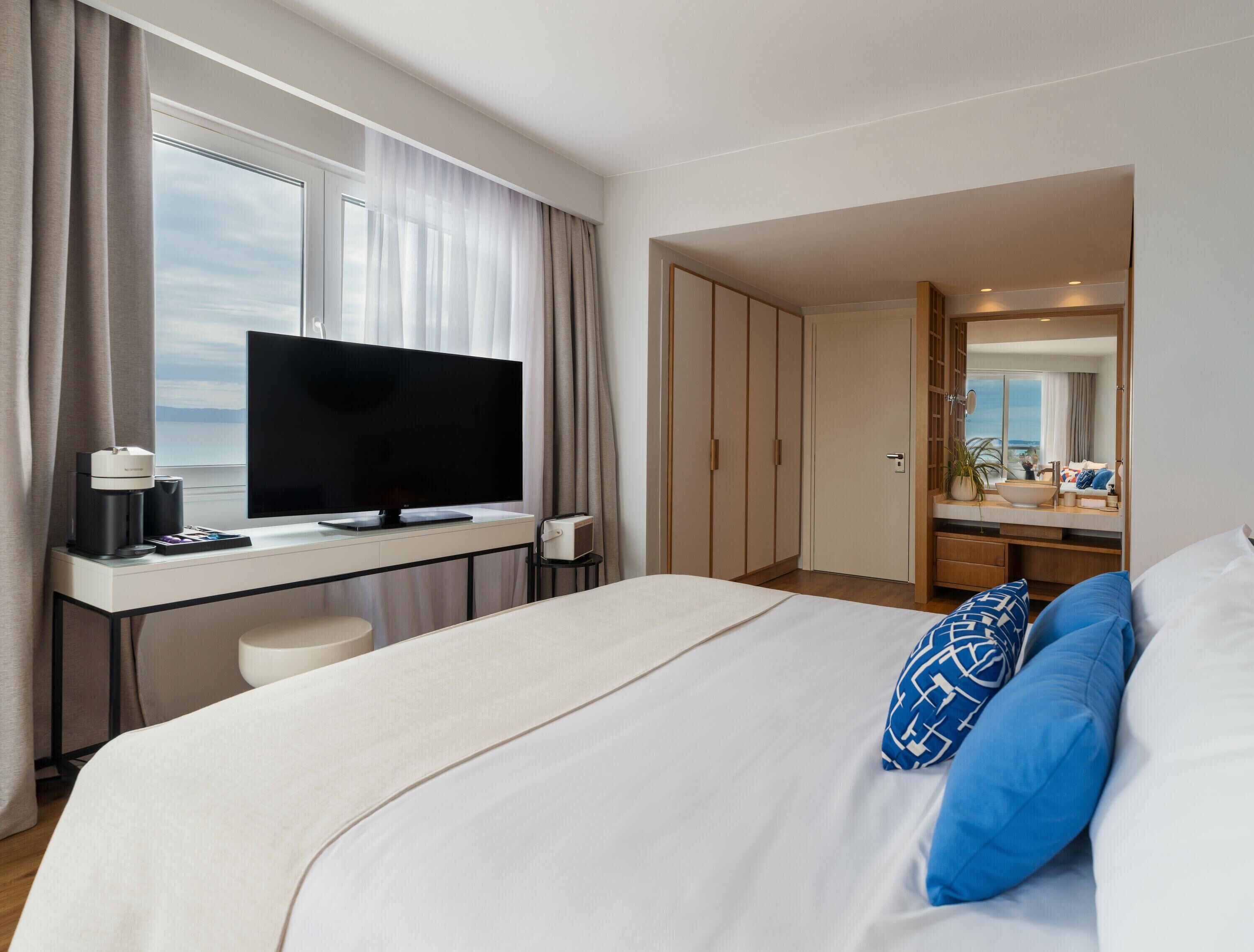 A hotel room with a bed, a desk with a TV, a coffee maker, and a bathroom with a mirror and sink.