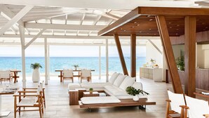 A spacious, open-plan living area with a view of the sea, featuring a wooden ceiling, white furniture, and a modern design.