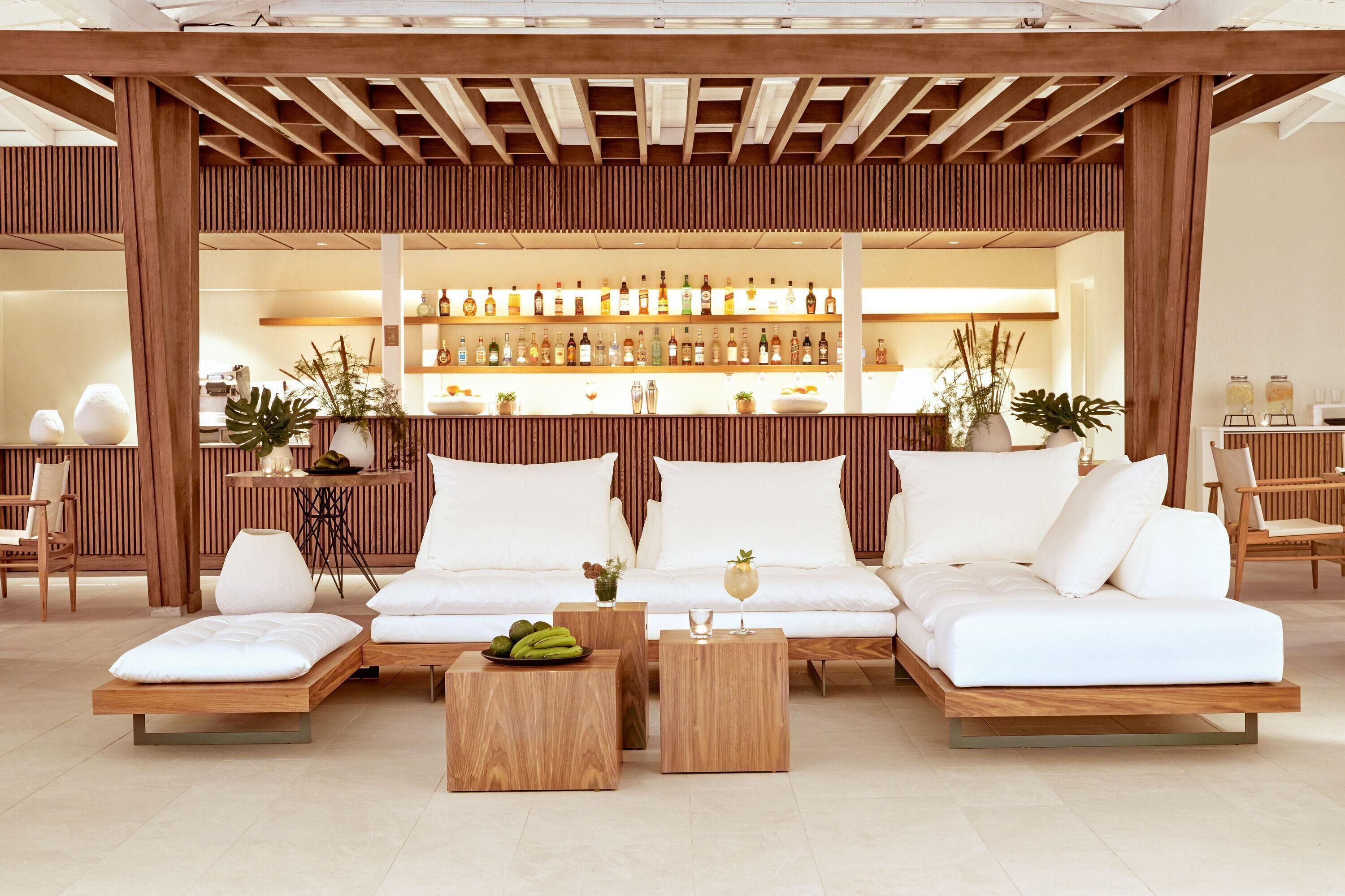 A modern lounge area with a wooden ceiling, a white sofa set, and a bar with various bottles.