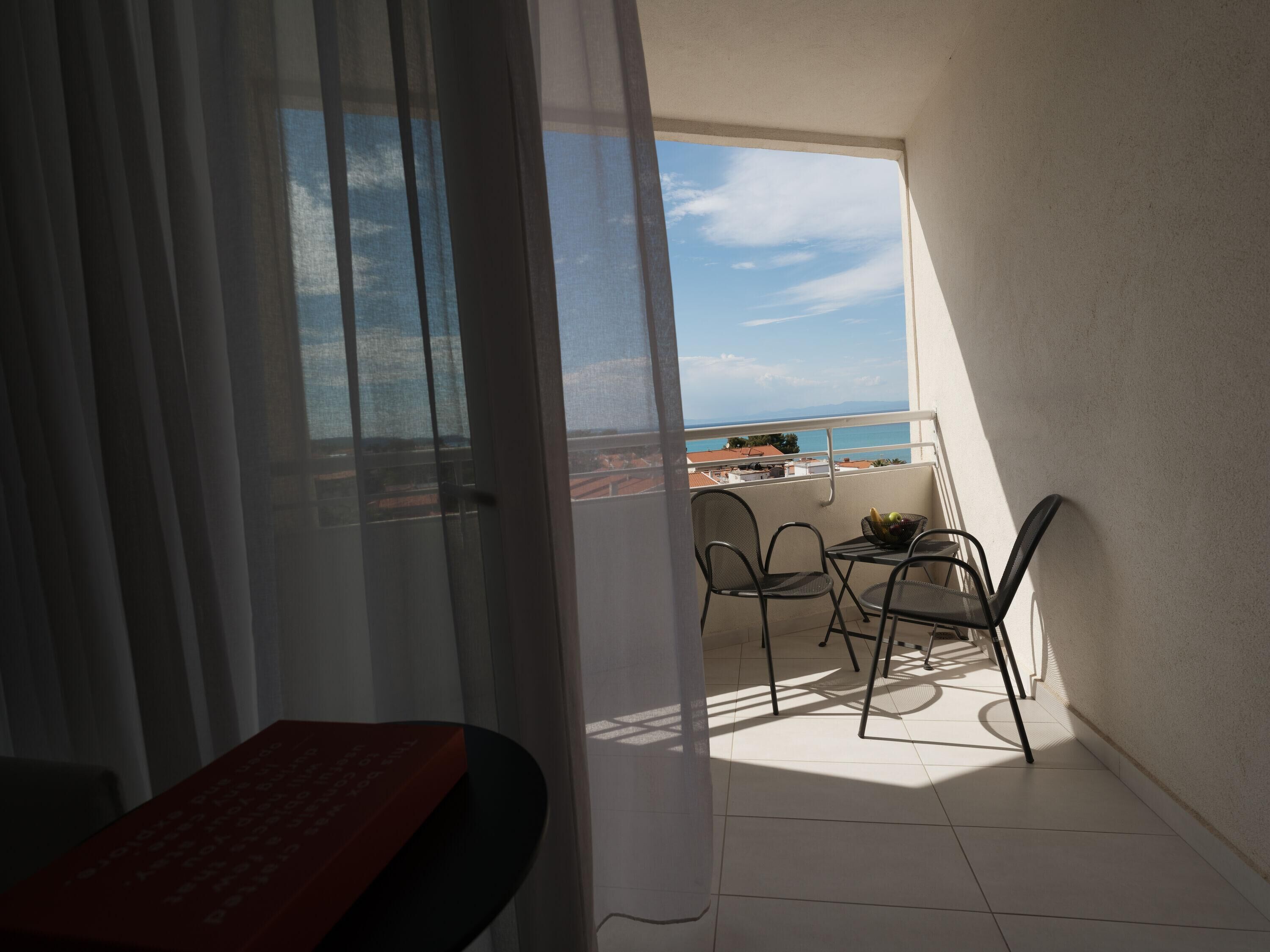 Un balcón con mesa y sillas, vista al mar y cielo despejado.