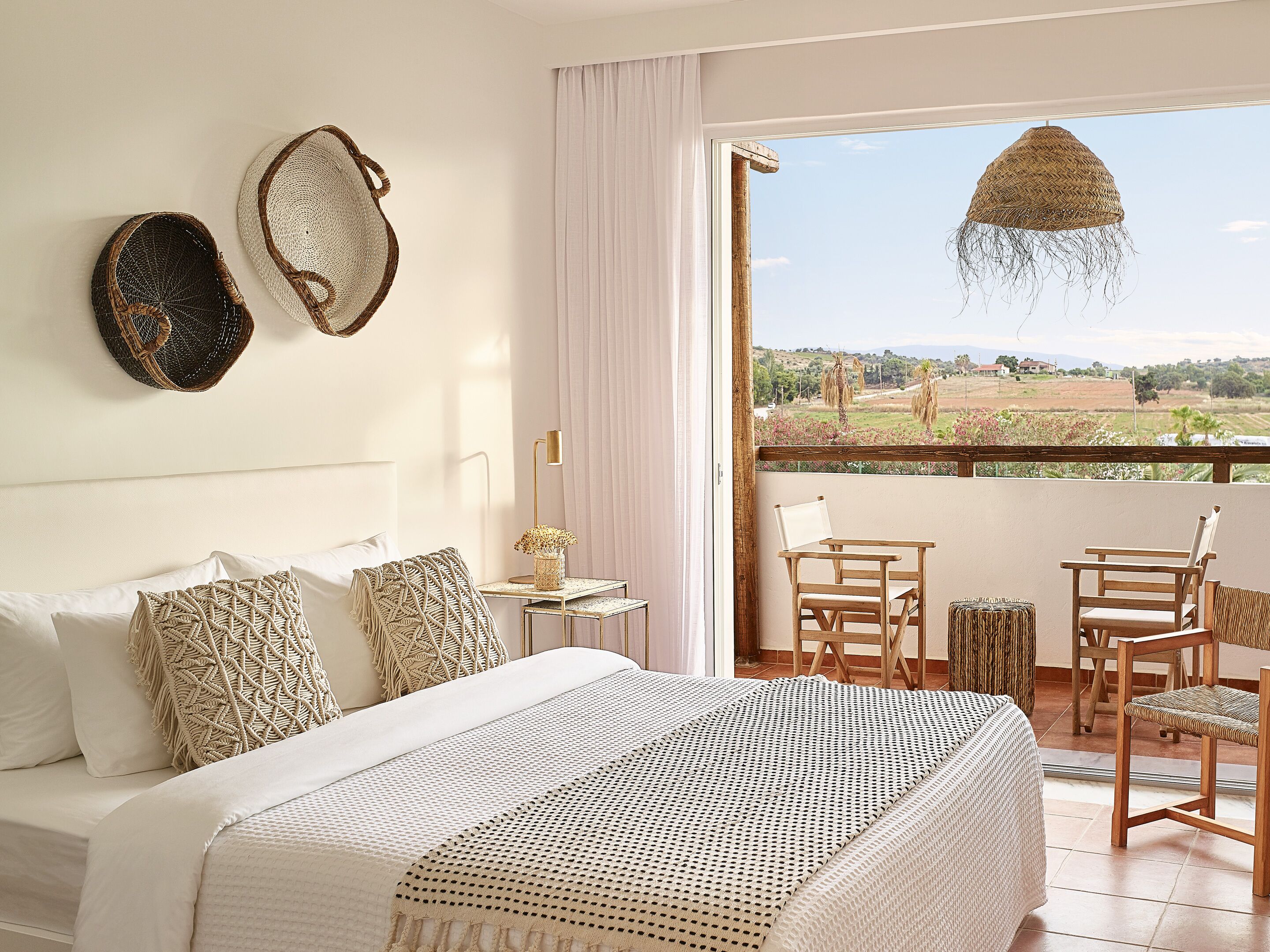 A bedroom with a large bed, a nightstand, a lamp, and a view of the outdoors through a balcony.
