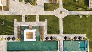 Vista aérea de um resort com uma piscina central, várias piscinas menores e área ajardinada com caminhos e vegetação.