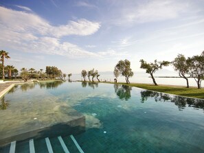 A clear infinity pool with a view of the sea and palm trees. - Grecotel Casa Marron (West Achaea)