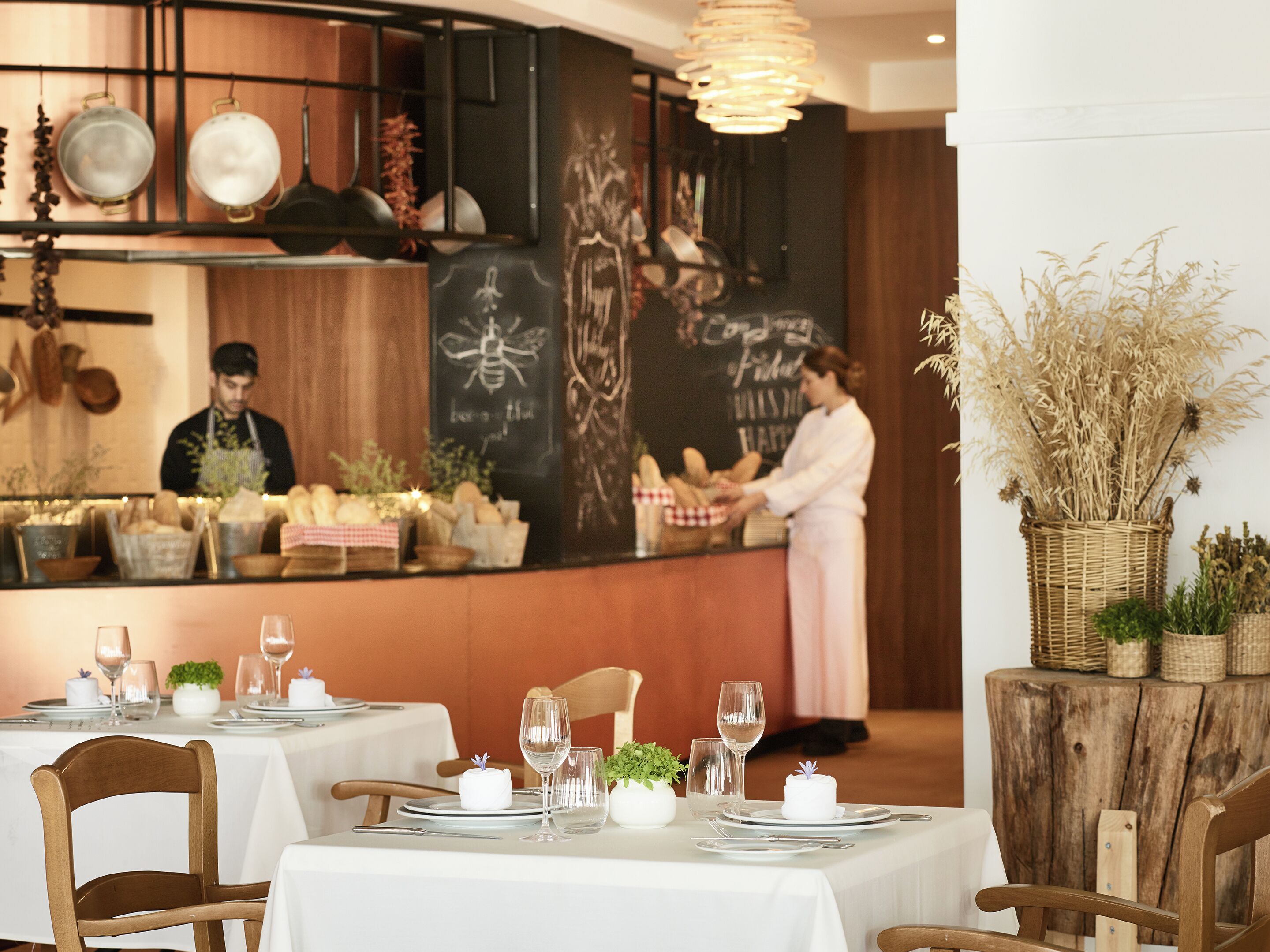 Un restaurante con mesas dispuestas para comer, un chef preparando comida y un menú en una pizarra.