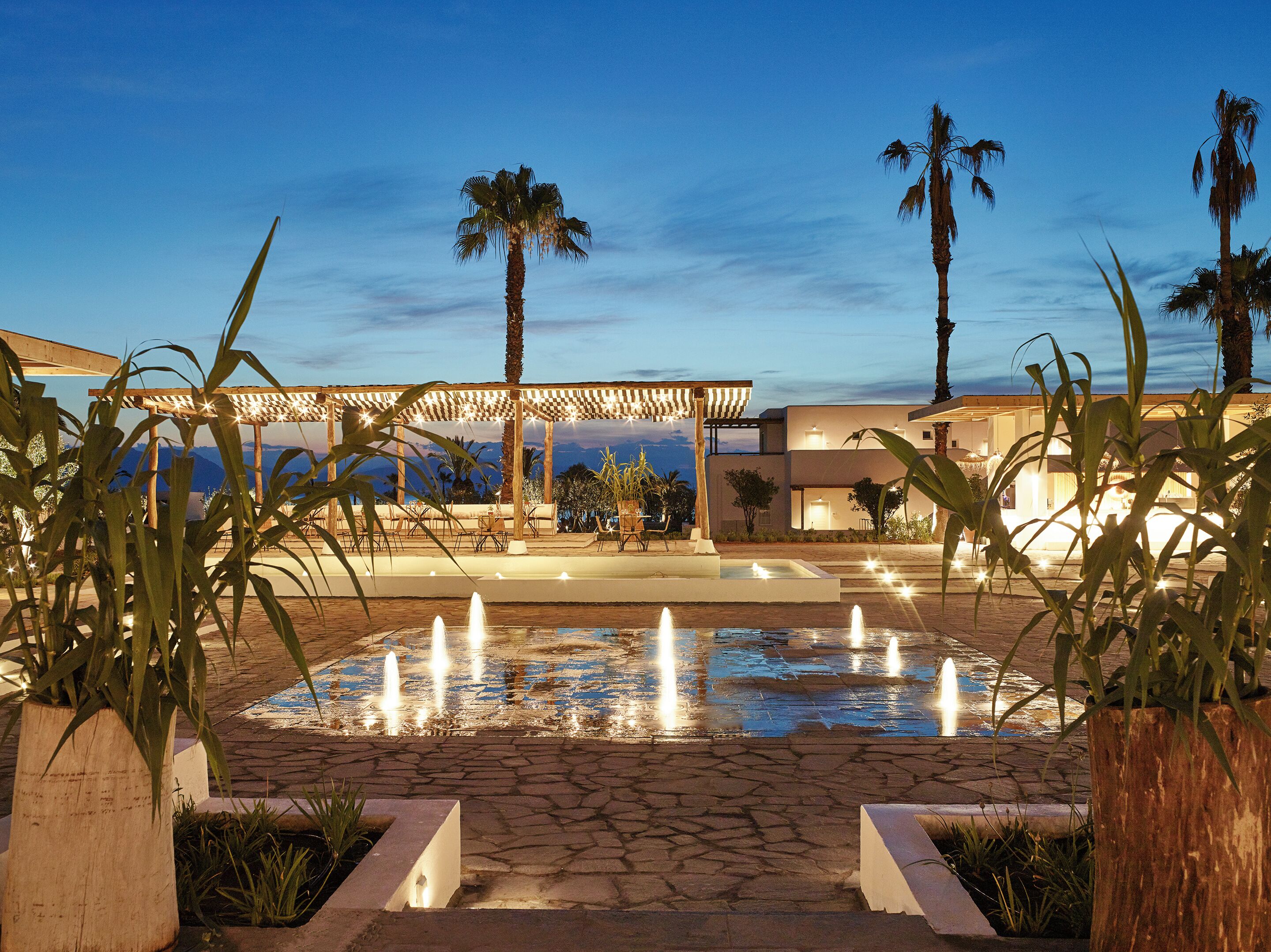 A pool area with a pergola, palm trees, and a view of the mountains.