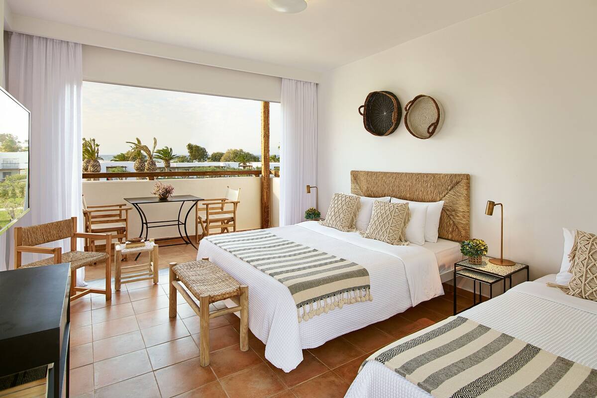 A hotel room with a bed, a small table with chairs, a balcony with a view, and a TV.
