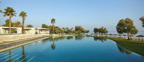A swimming pool with lounge chairs and palm trees, surrounded by a clear sky and a view of the sea.