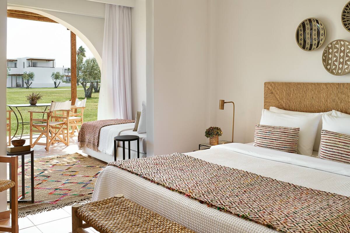 A bedroom with a large bed, a small table, chairs, and a view of the outdoors.