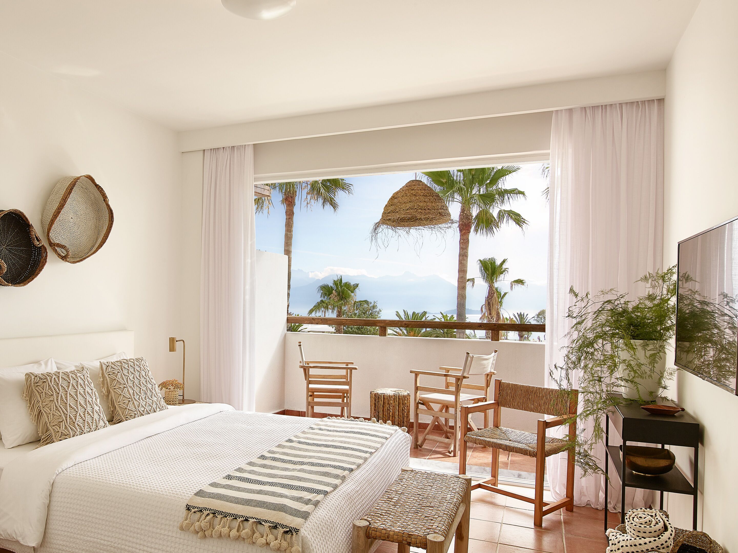 A bedroom with a bed, a balcony with a view, and a TV.