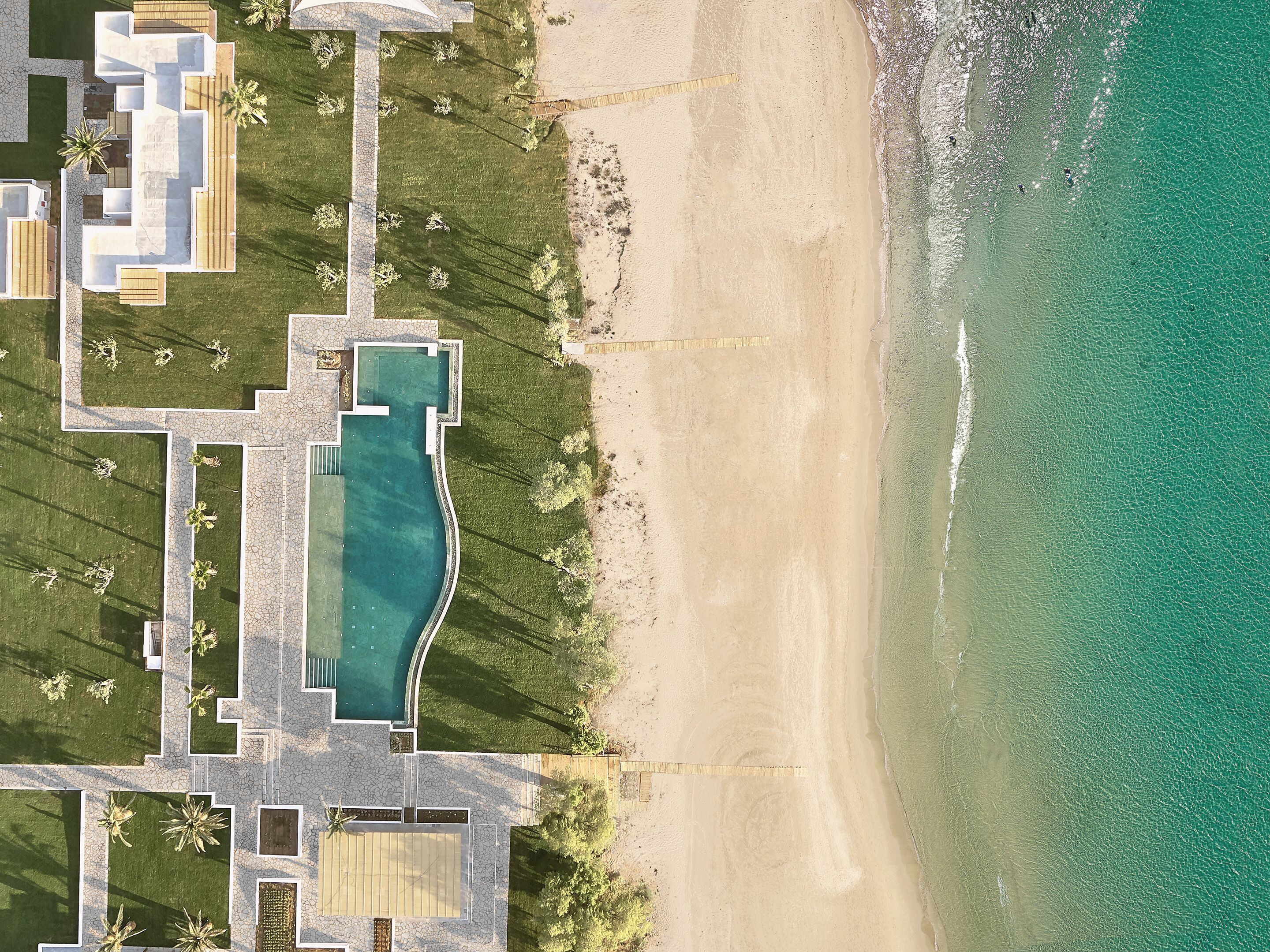 An aerial view of a coastal property with a swimming pool, beachfront, and landscaped areas.