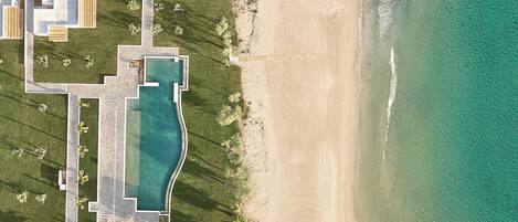 Vista aérea de una propiedad costera con piscina, acceso directo a la playa y zonas ajardinadas.