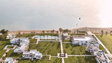 An aerial view of a resort with multiple white buildings, a central pool area, and a beach in the background.