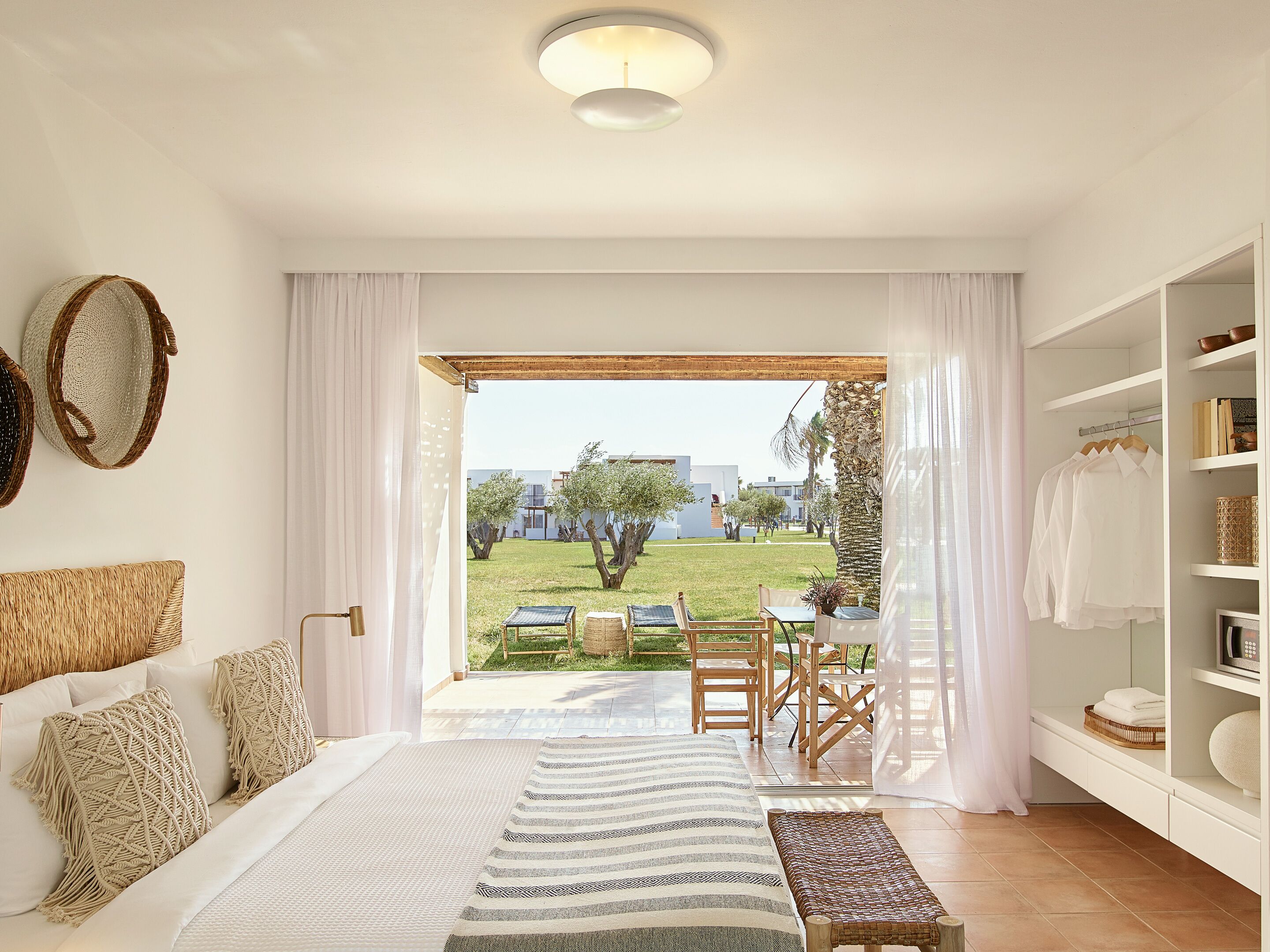 A bedroom with a bed, a bedside table, a wardrobe, and a view of an outdoor garden.