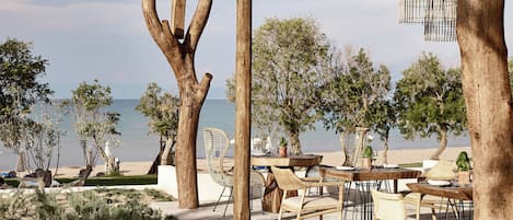 An outdoor seating area with wooden tables and chairs, surrounded by trees and overlooking a body of water.