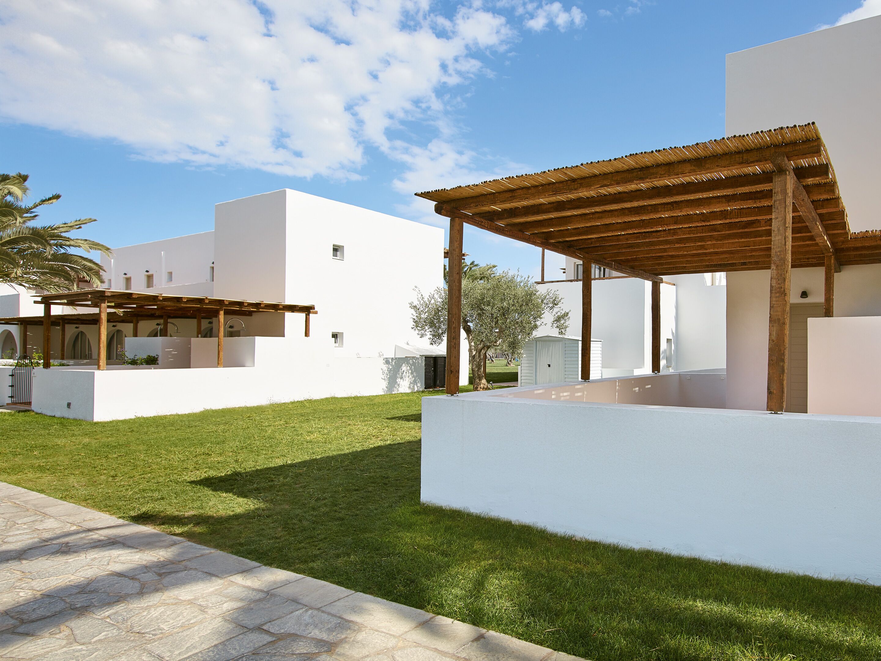 Un espace extérieur moderne, aménagé en patio, avec une pergola, un petit jardin et un bâtiment blanc doté d’un toit plat.