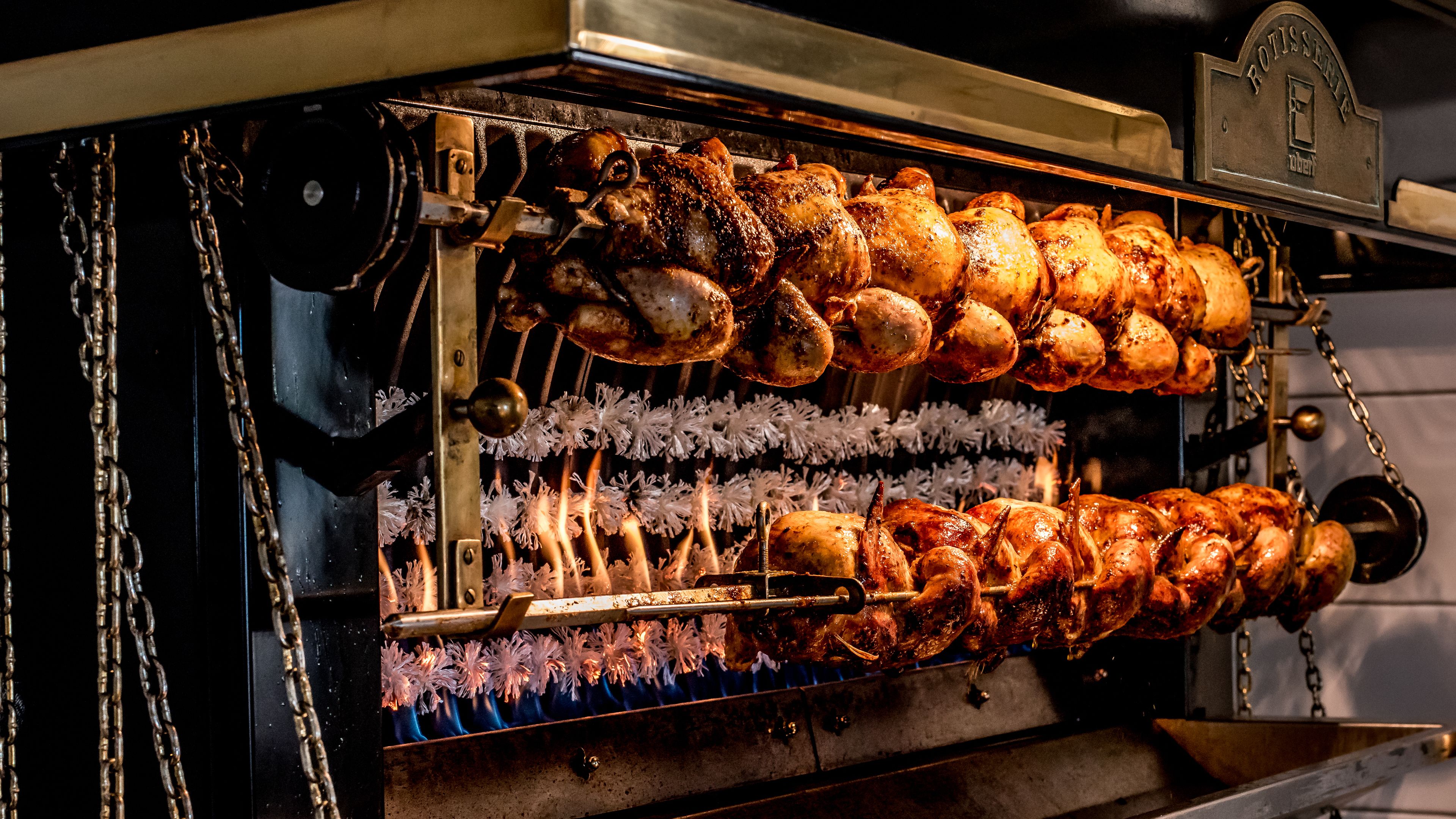 En roterende grill med flere kyllinger, der bliver stegt.
