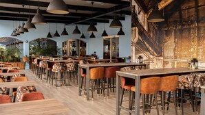 A modern restaurant interior with multiple dining areas, wooden tables, and chairs.