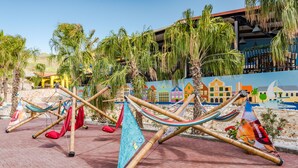 Hammocks strung between bamboo poles on a brick patio with palm trees and a colorful mural in the background.