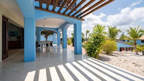 A spacious covered patio with a dining area, blue walls, and a view of palm trees and a building in the background.