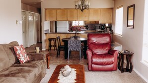 Una sala de estar con un sofá, un sillón de cuero rojo, una mesa de centro con un cuenco decorativo, y una zona de comedor con una mesa y sillas.