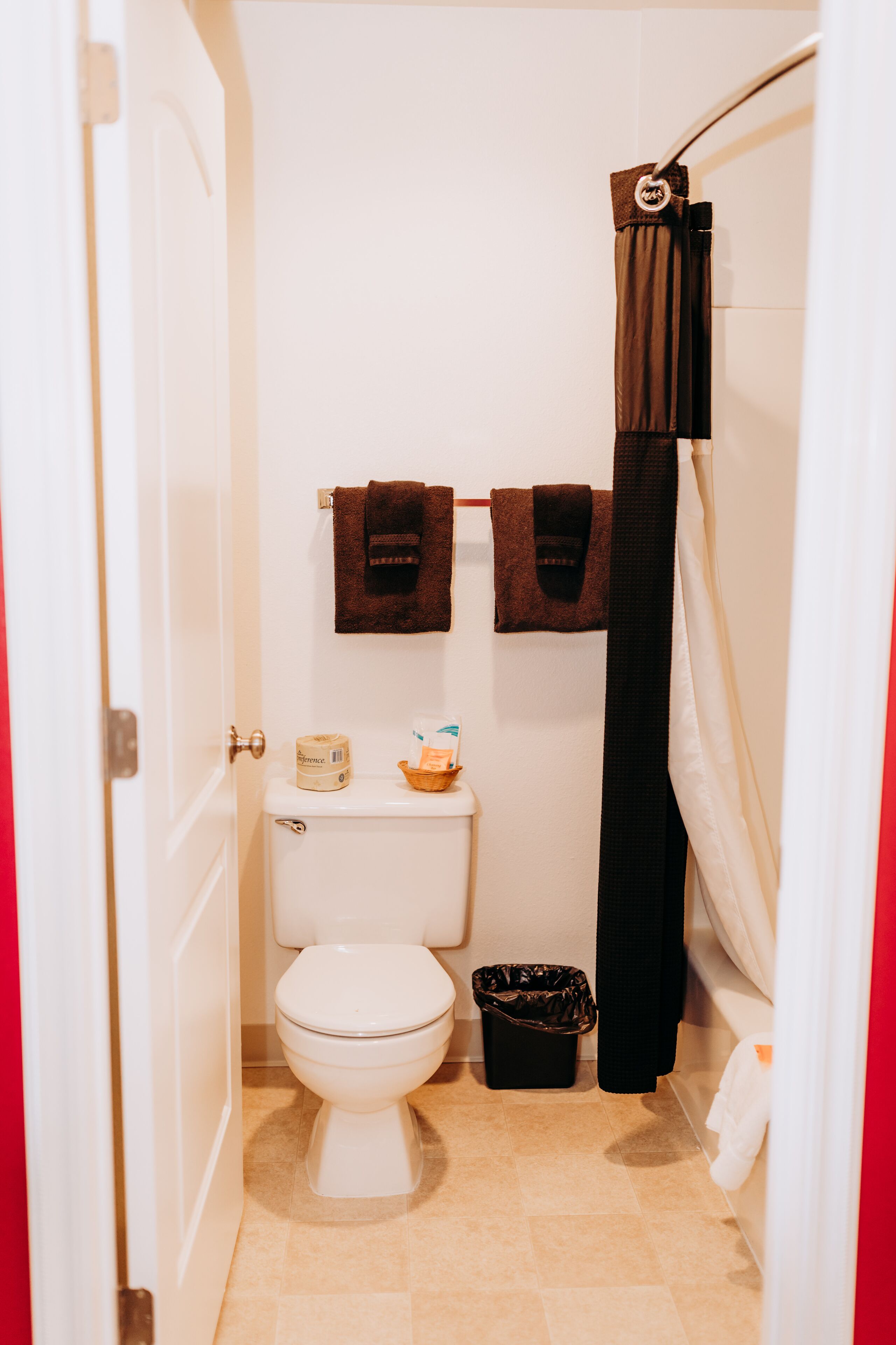 Une petite salle de bain avec des toilettes, une poubelle et un rideau de douche.