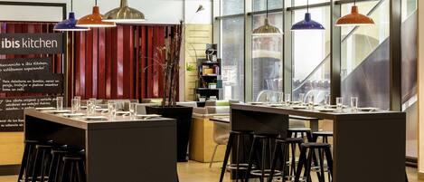 A modern kitchen area with bar stools, pendant lights, and a large window providing natural light.