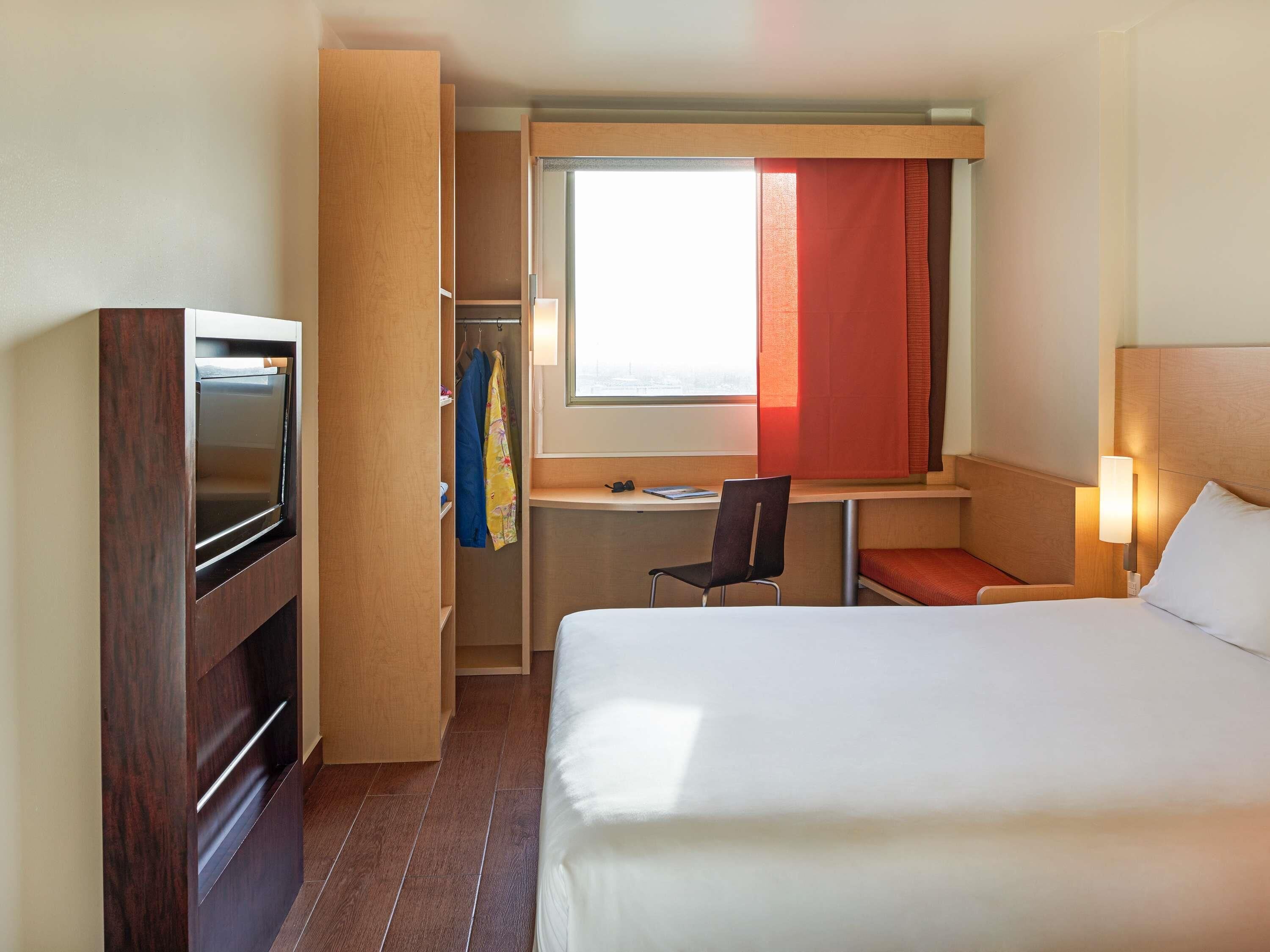 Una habitación de hotel con cama, escritorio, silla, televisor y armario.