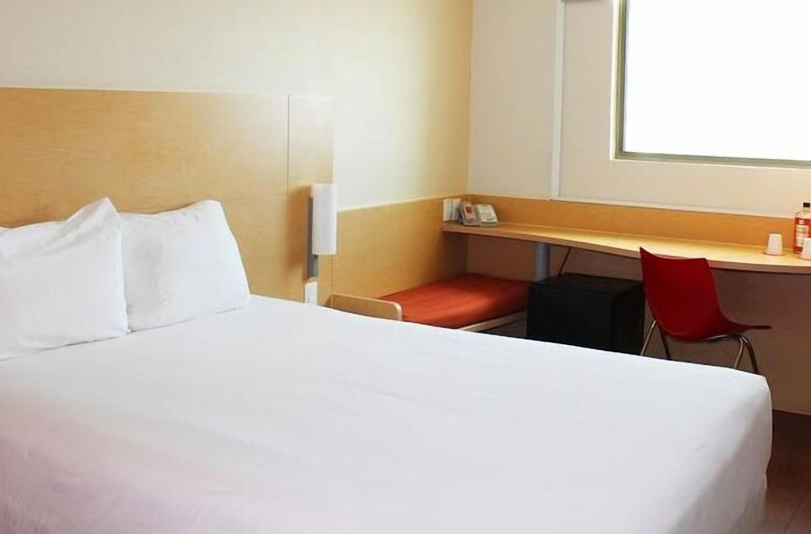 A hotel room with a bed, a desk, a chair, and a window.