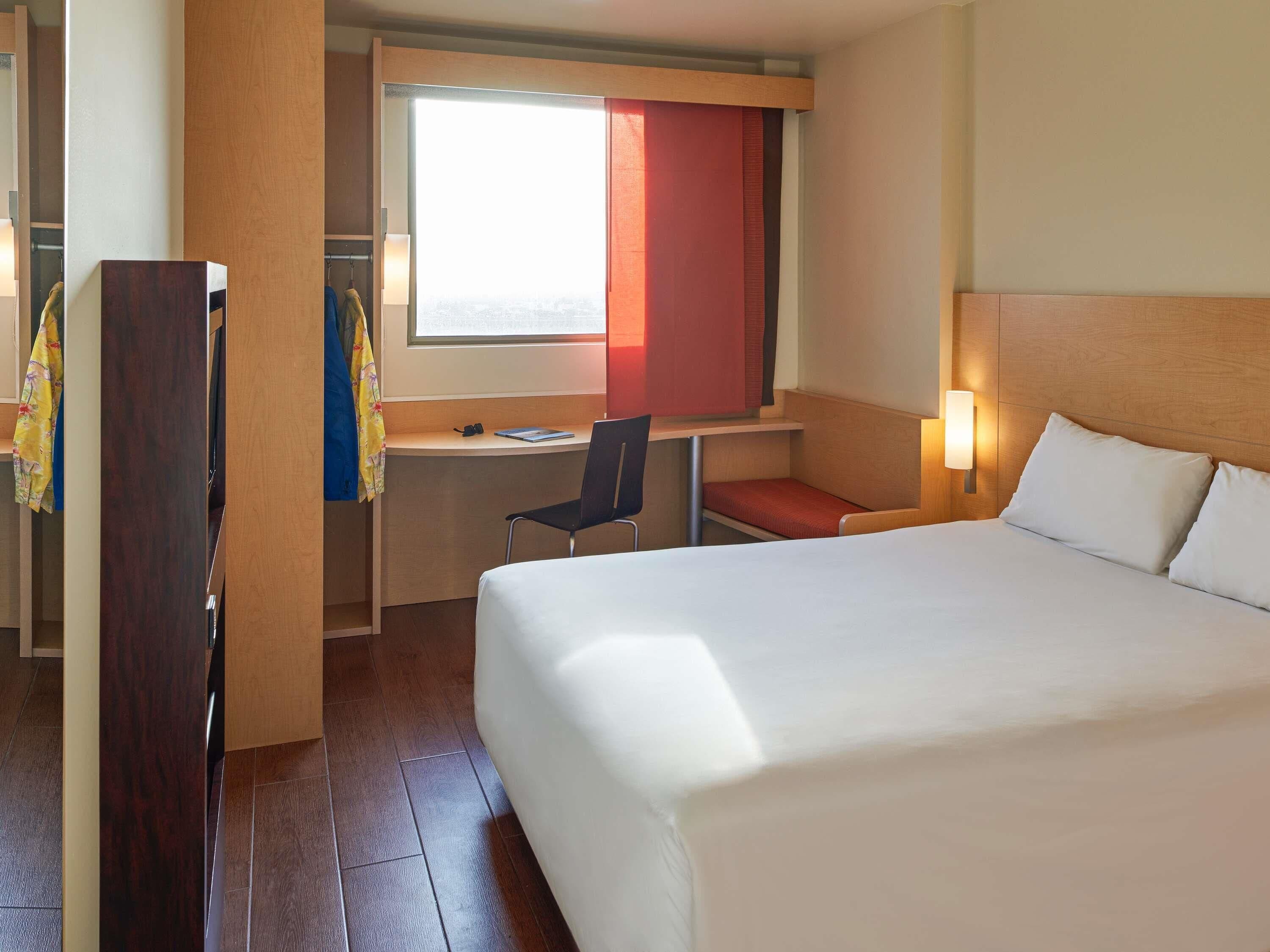 Une chambre d’hôtel avec un lit, un bureau, une chaise et une fenêtre avec des rideaux.