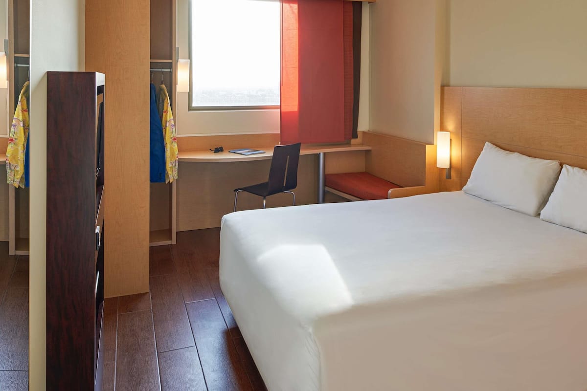 Une chambre d’hôtel avec un lit, un bureau, une chaise et une fenêtre avec des rideaux.