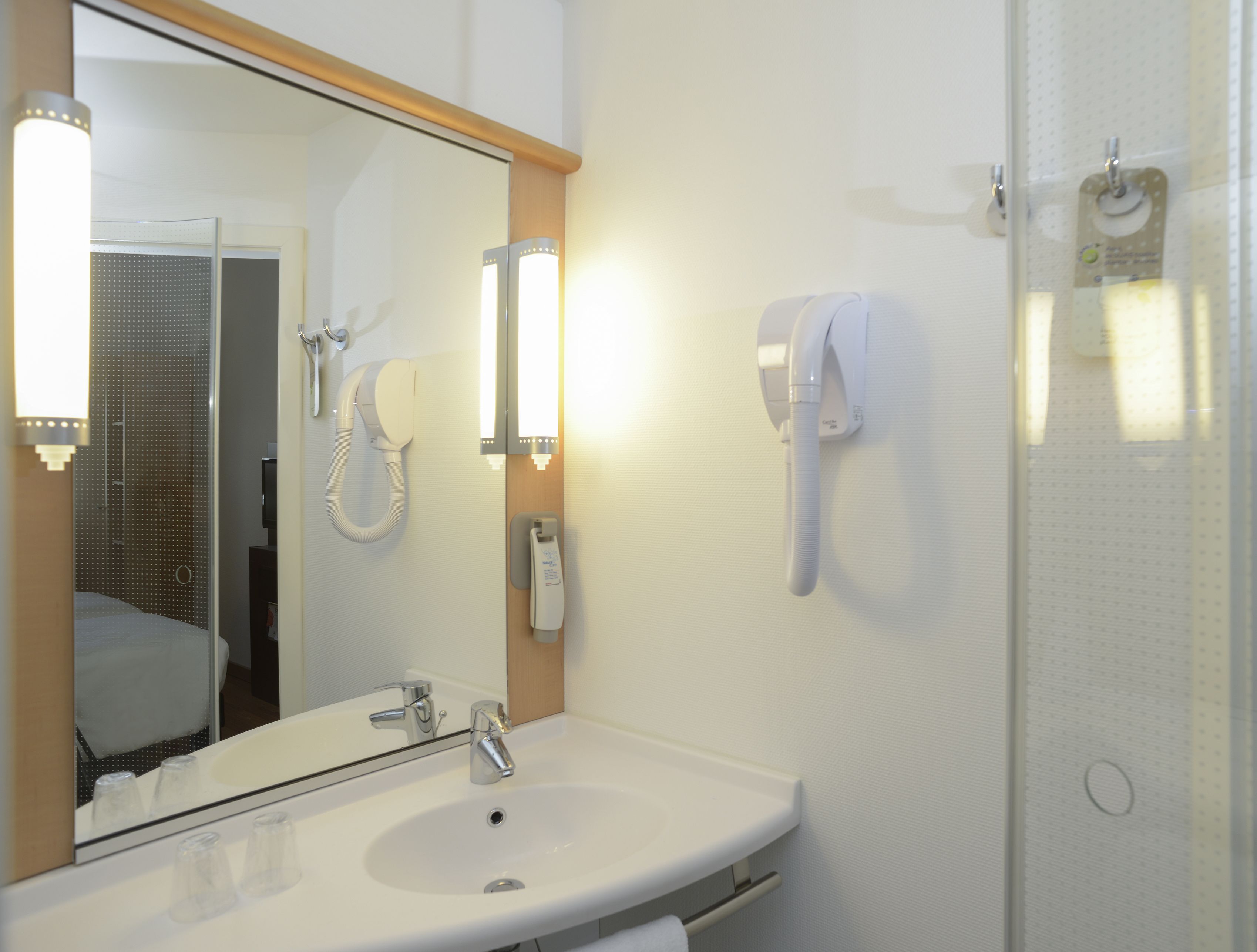 A bathroom with a white sink, a mirror, and two white hand dryers mounted on the wall.