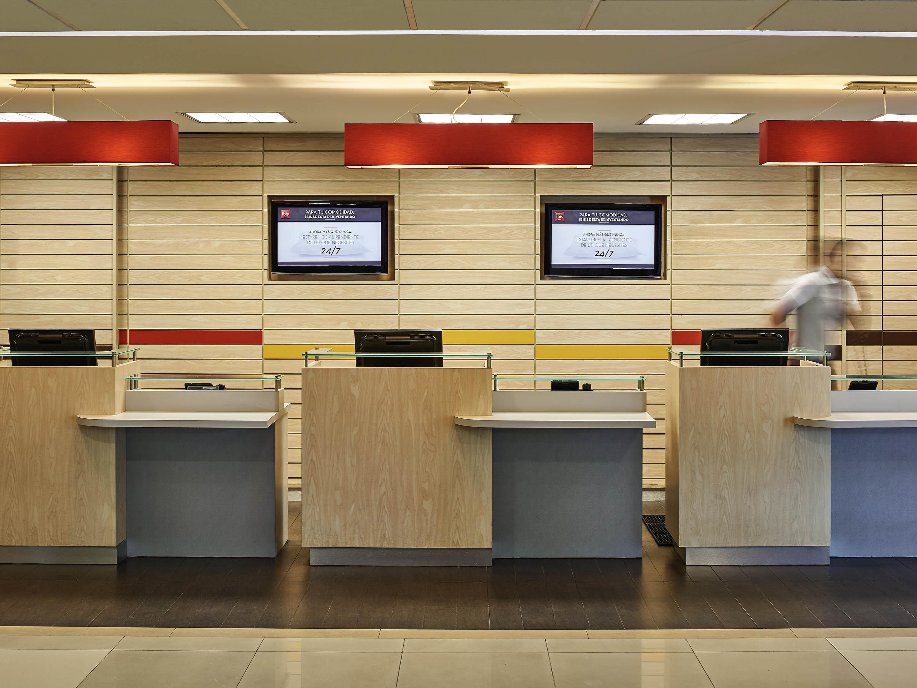 A reception area with wooden paneling, glass counters, and digital screens displaying a 24/7 message.