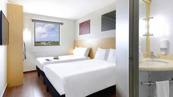 Ein Hotelzimmer mit zwei Betten, einem großen Fenster mit Blick auf die Stadt, einem Badezimmer mit Waschbecken und Spiegel sowie einem Handtuchhalter.