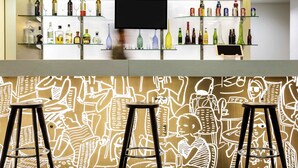 Uma área de bar com banquetas, uma tela de televisão e prateleiras com diversos frascos.