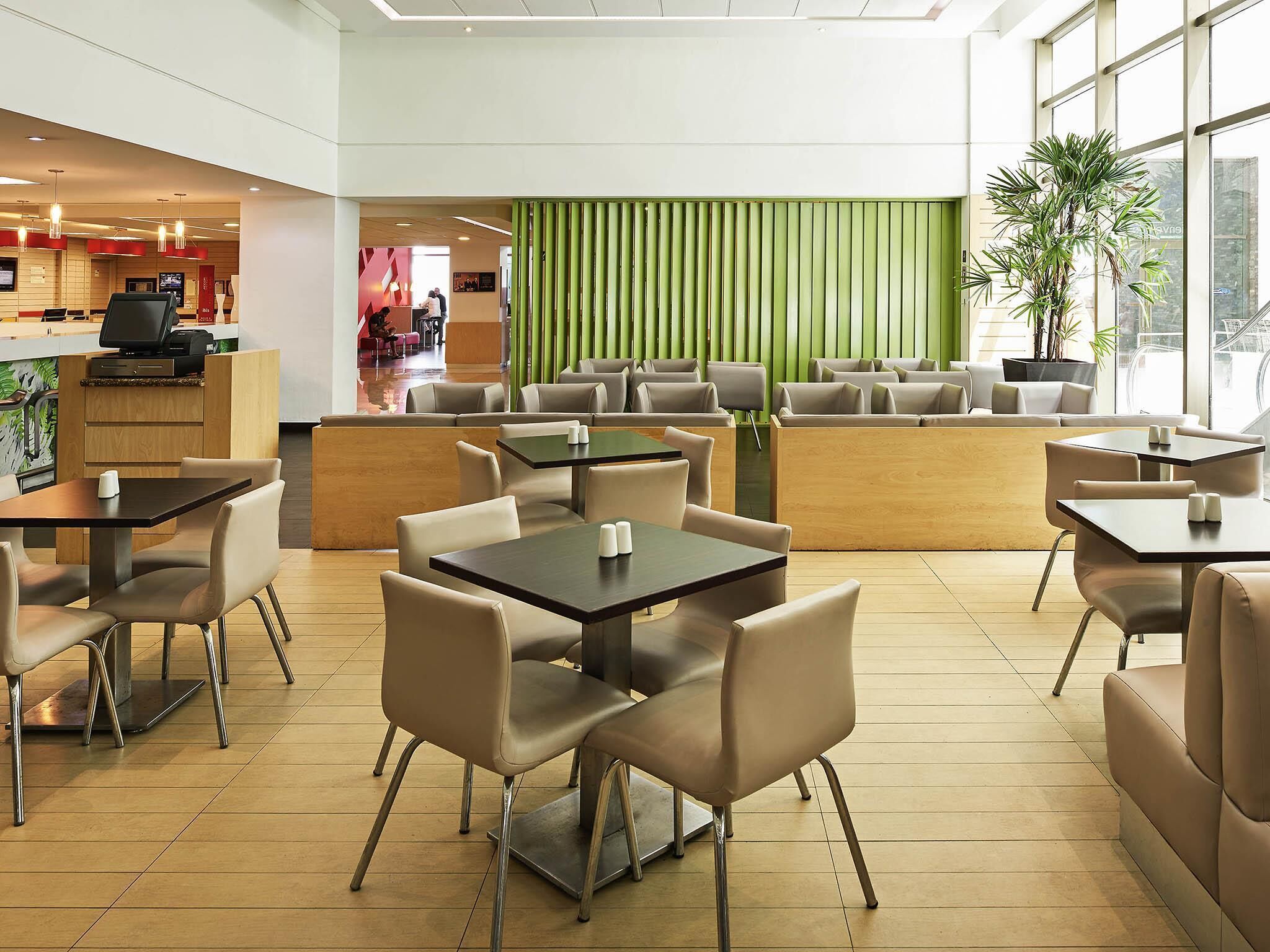 Un restaurante moderno con una separación verde, suelo de madera y diversas opciones de asientos, incluyendo mesas y cabinas.